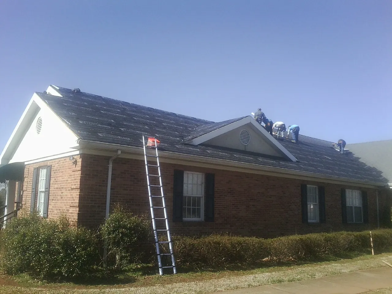 Crew tearing shingles off a brick ranch roof with a ladder set — Emergency Roof Repair work by our crew in Valley
