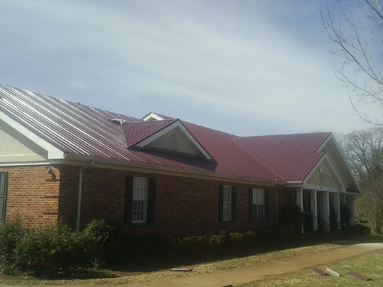 Red metal roof with gabled entries on a long brick building, from a Hail Damage Roof Repair job in Valley